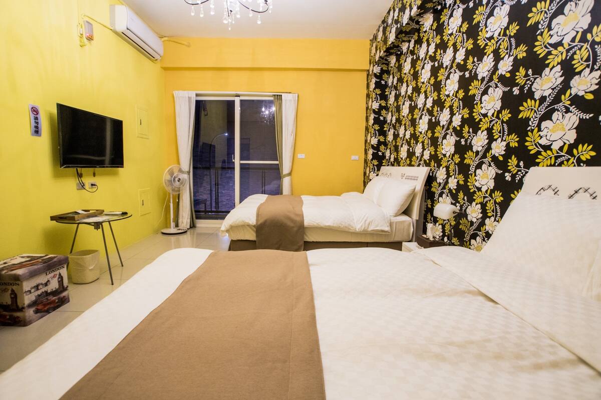 A hotel room with a bed, a television, a fan, and a window with curtains.