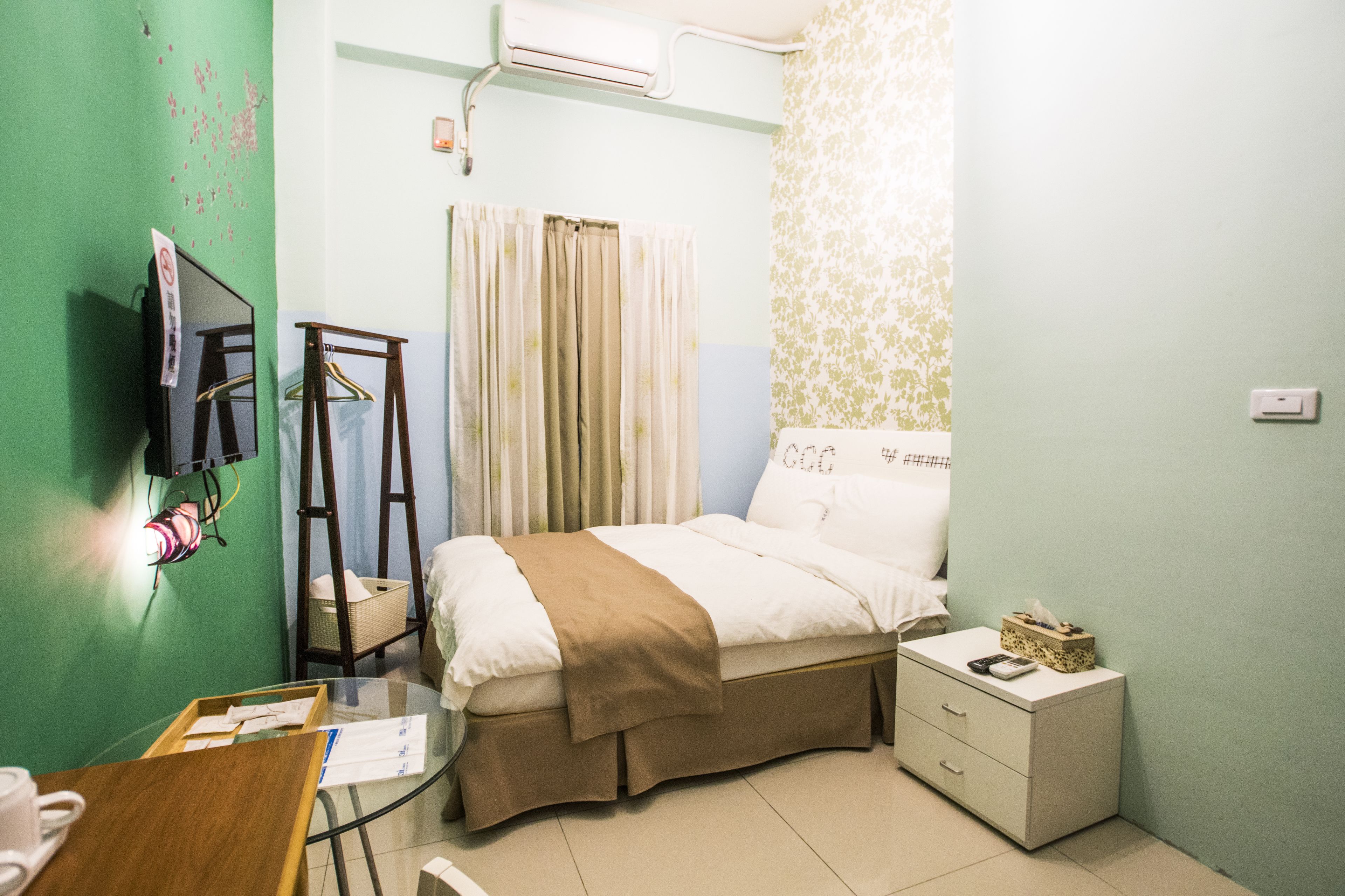 A hotel room with a bed, bedside table, and a desk with a chair.
