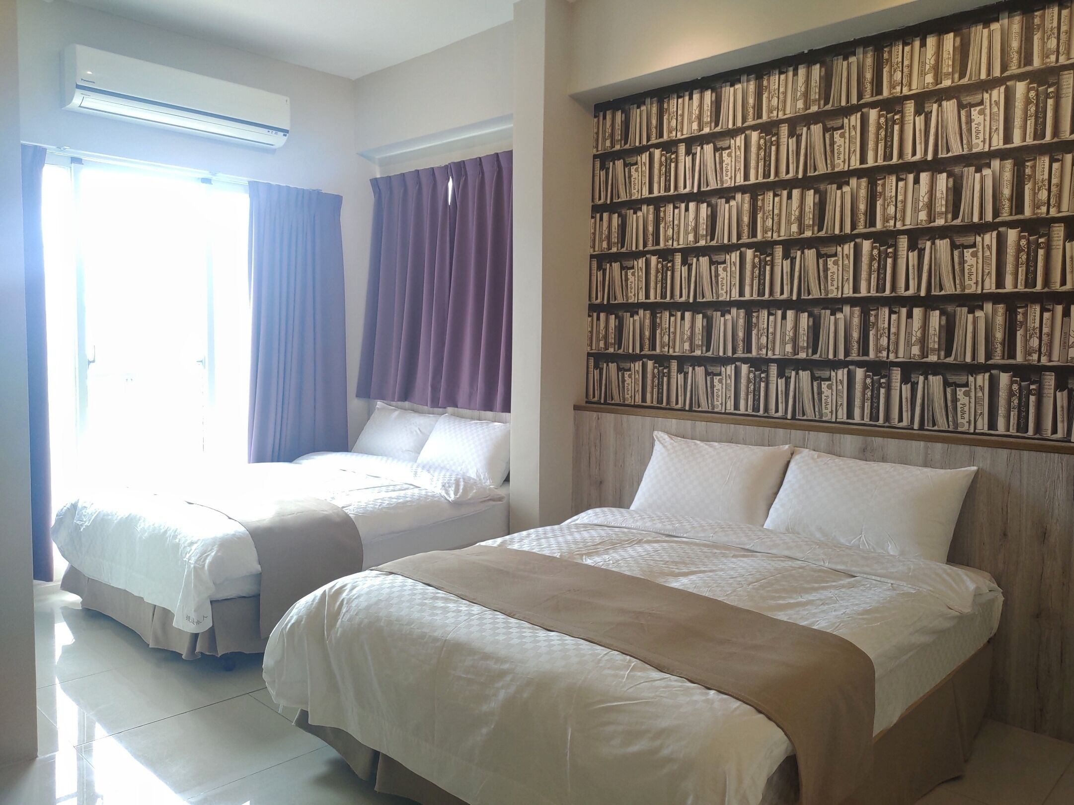 Una habitación de hotel con dos camas, una amplia estantería y un aire acondicionado.