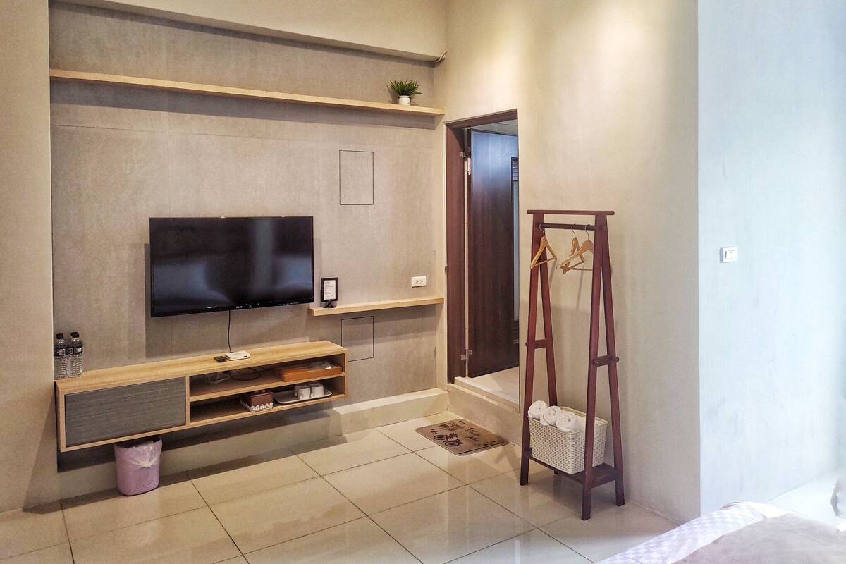 A modern living room with a flat-screen TV mounted on a wall, wooden entertainment unit below, and a wooden hanger rack with towels.