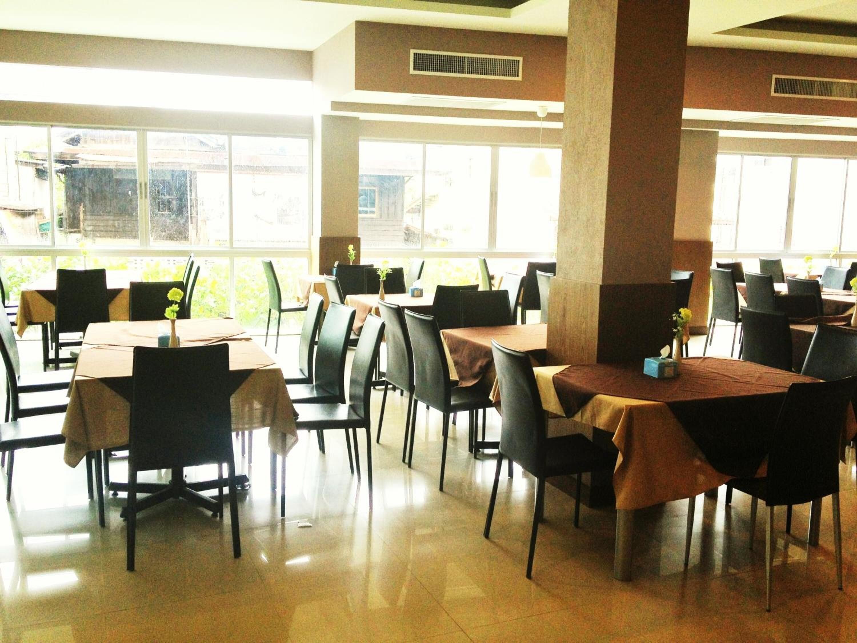 Un comedor amplio con múltiples mesas y sillas, ventanas grandes que dejan entrar luz natural y un piso limpio con azulejos.