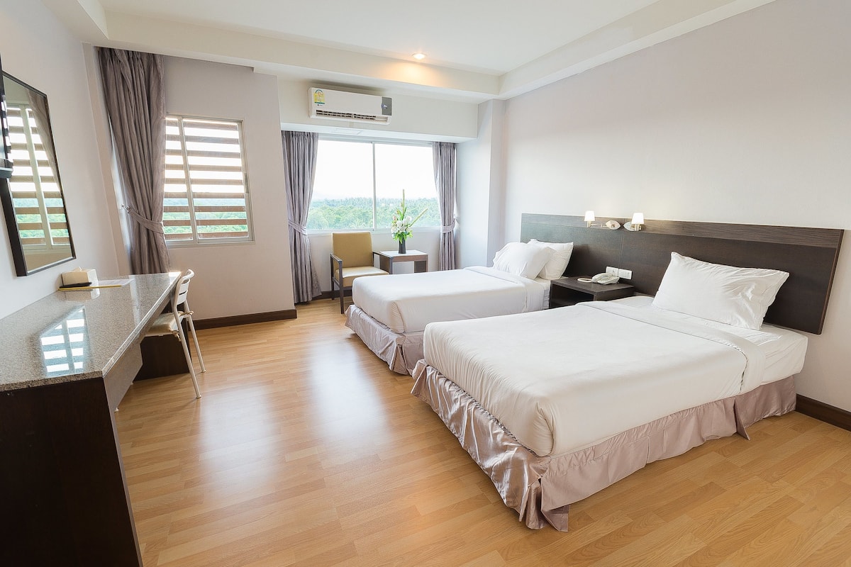 Habitación de hotel con dos camas, un escritorio y una ventana con cortinas.
