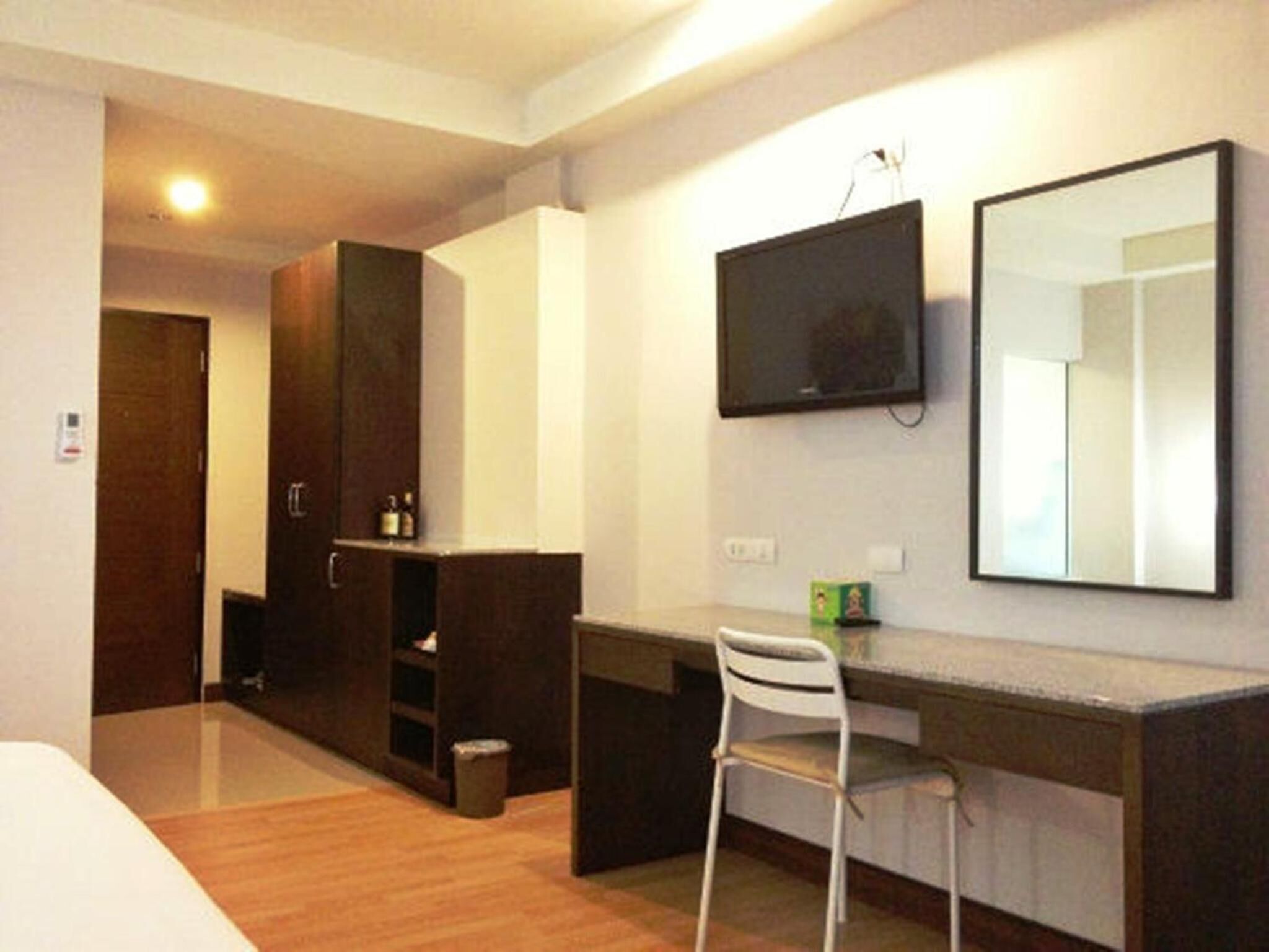 Habitación de hotel con cama, escritorio con silla, armario, televisor montado en la pared y un pequeño cubo de basura.