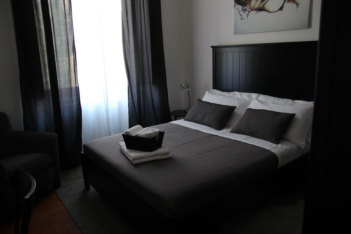 Una camera d'albergo con un letto grande, un comodino, una sedia e un quadro appeso al muro.