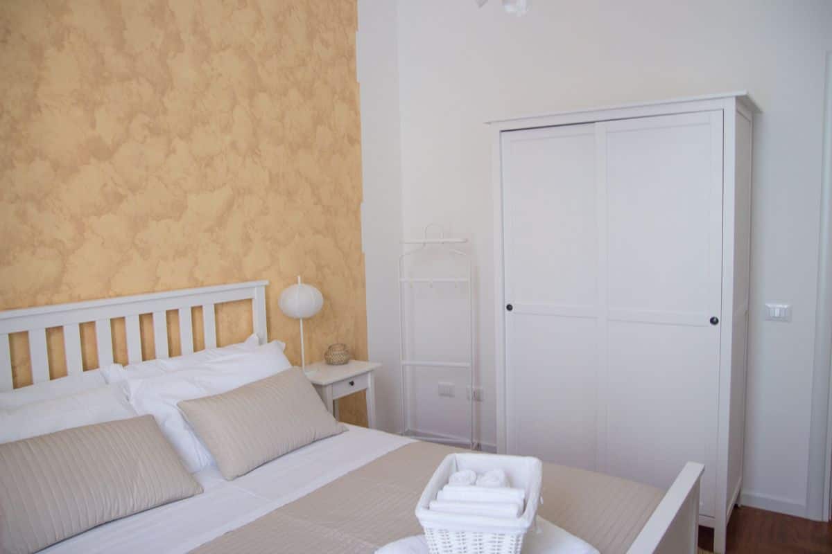 Una camera da letto con un letto, un comodino con una lampada, un armadio e un cesto per la biancheria.