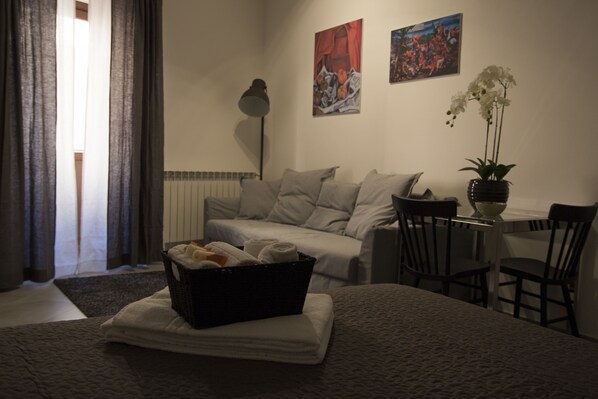 A hotel room with a bed, a small table with chairs, a lamp, a plant, and artwork on the wall.