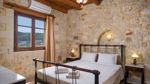 Une chambre aux murs de pierre, avec un lit, deux lampes de chevet et un appareil de climatisation.
