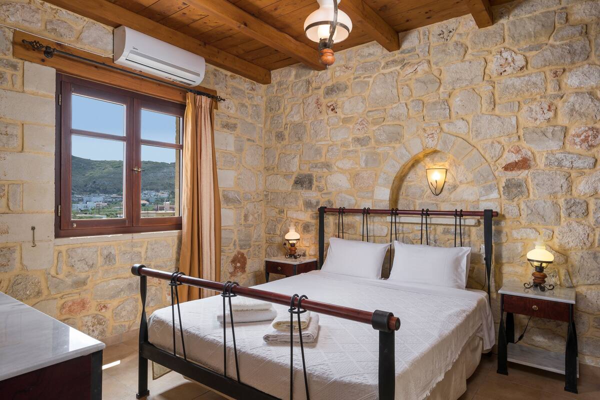 Ein Schlafzimmer mit Steinwänden, einem Bett, zwei Nachttischlampen und einer Klimaanlage.