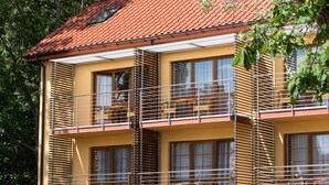 A multi-story building with a red-tiled roof, balconies with metal railings, and windows with blinds. - Willa Florek (Rewal)