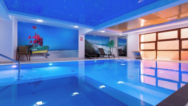 An indoor swimming pool with a starry ceiling, lounge chairs, and a mural of a beach scene. - Willa Florek (Rewal)