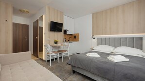 A modern hotel room with a bed, a desk with a chair, a television, and a wardrobe. - Willa Florek (Rewal)