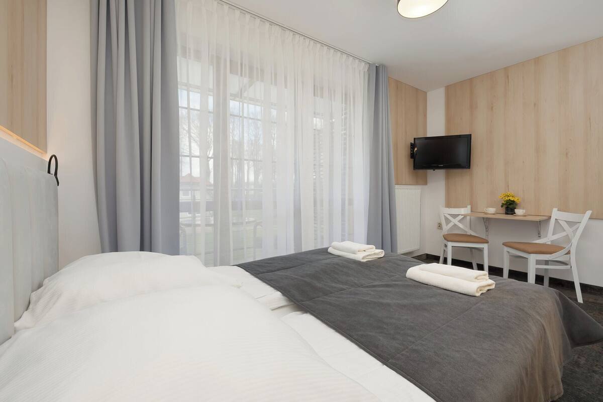 A hotel room with a bed, a desk with a chair, a TV, and a window with curtains.