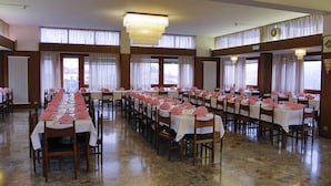 Een ruime balzaal met meerdere tafels gedekt voor een diner, met witte tafelkleden en roze servetten.