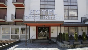 Een hotelentree met een grindbestrating, een overdekt gedeelte met potplanten, en een bord boven de entree met de tekst 'HOTEL VALLERINI'.