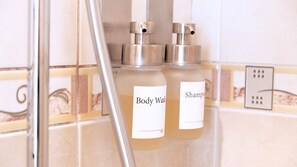 Two bottles of body wash and shampoo in a bathroom with tiled walls and a showerhead. - Moon Villa B&B (Taitung)