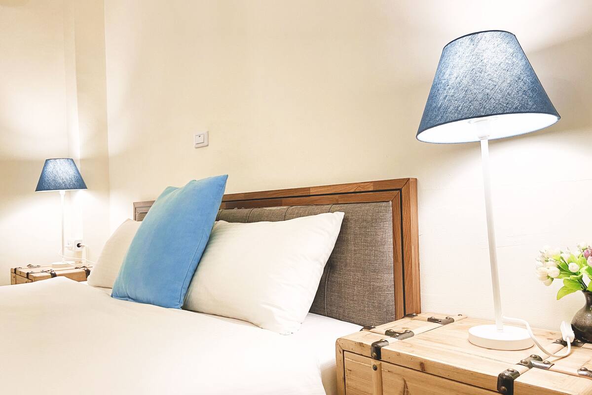 A neatly made bed with a wooden headboard, two bedside lamps, a wooden nightstand, and a small table with a vase of flowers.
