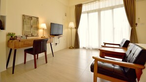 Una habitación de hotel con un escritorio de madera, televisión, sofá y una ventana grande con cortinas.
