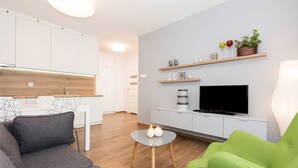 A modern living room with a grey sofa, a green armchair, a flat-screen TV, and a small round table with two candles. - Apartamenty Florek - Morski (Kolobrzeg)