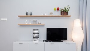 A modern living room with a flat-screen TV, a white cabinet, and two wooden shelves with decorative items. - Apartamenty Florek - Morski (Kolobrzeg)