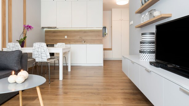 A modern kitchen with white cabinets, a dining area with a table and chairs, and a living area with a sofa and a TV. - Apartamenty Florek - Morski (Kolobrzeg)
