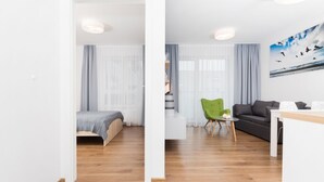 A modern hotel room with a wooden floor, a bed, a green chair, a sofa, and a painting of birds on the wall. - Apartamenty Florek - Morski (Kolobrzeg)