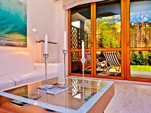 A modern living room with a glass coffee table, two candles, and a view of outdoor furniture through large glass doors.