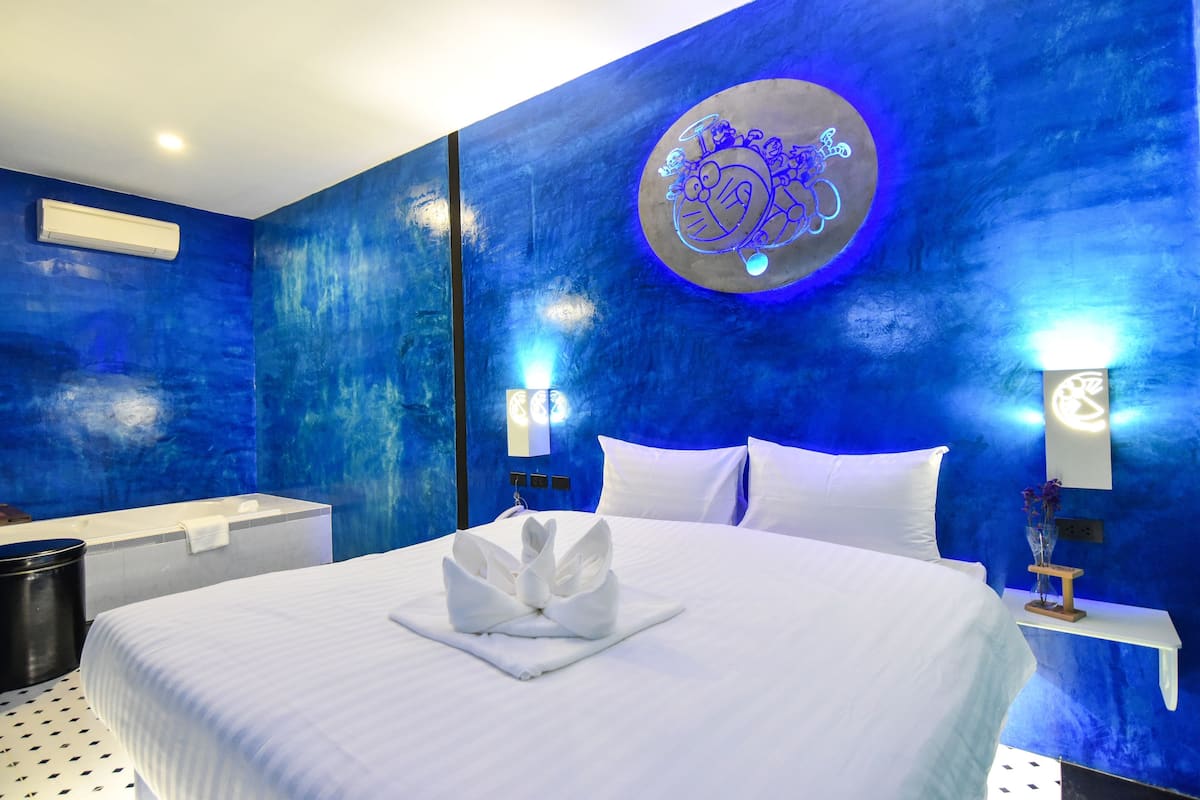 A hotel room with a bed, a wall-mounted air conditioner, a towel on the bed, and a neon sign on the wall.