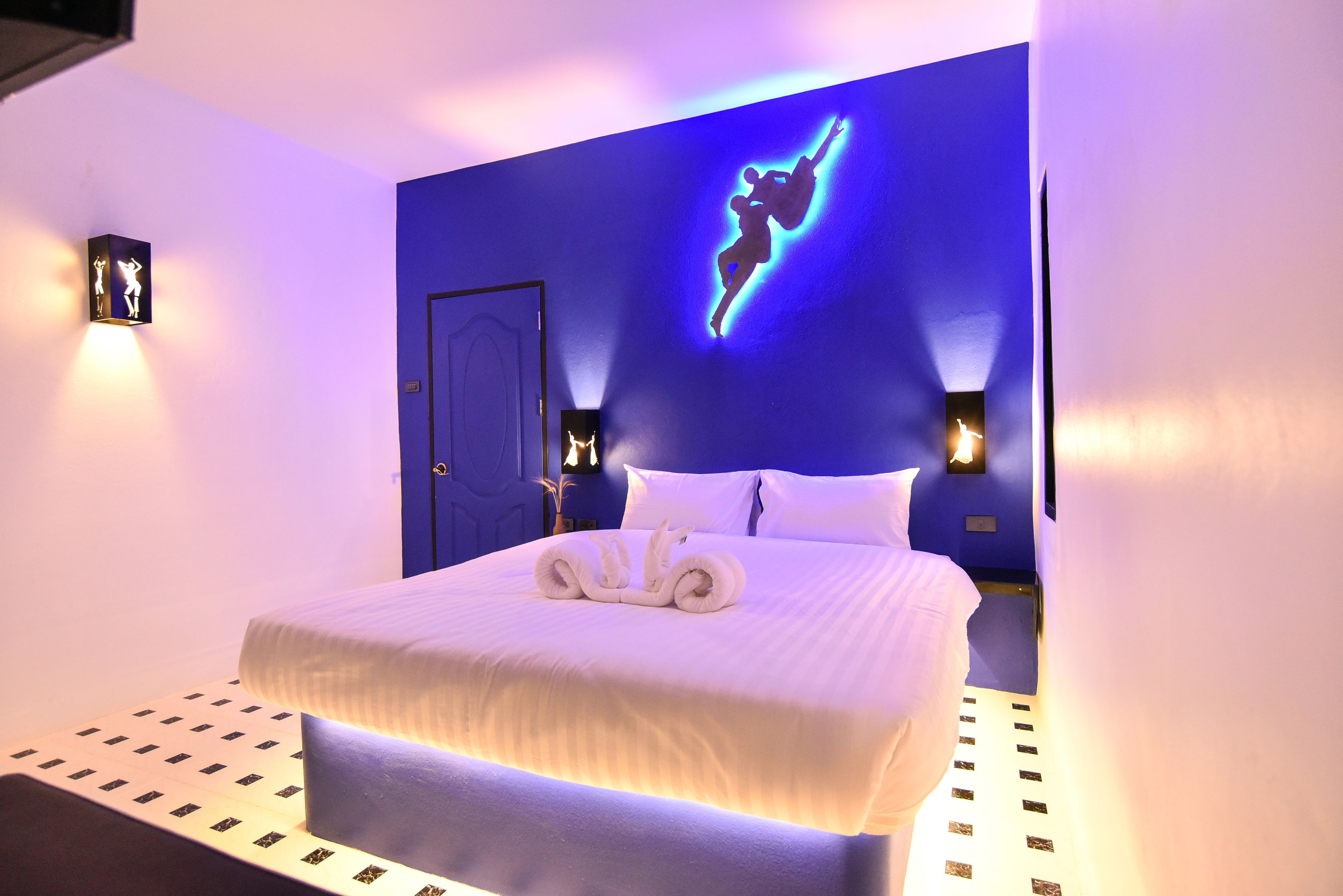 Habitación de hotel con una cama grande, una pared azul decorativa e iluminación empotrada.