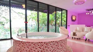 A modern bathroom with a mosaic-tiled bathtub, a large window with a view of greenery, and a cozy seating area with white furniture. - Bed Villa Resort Chaing Rai (Chiang Rai)