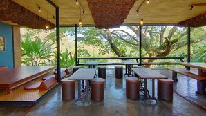 An outdoor dining area with tables and stools, surrounded by large windows offering views of trees and greenery. - Bed Villa Resort Chaing Rai (Chiang Rai)