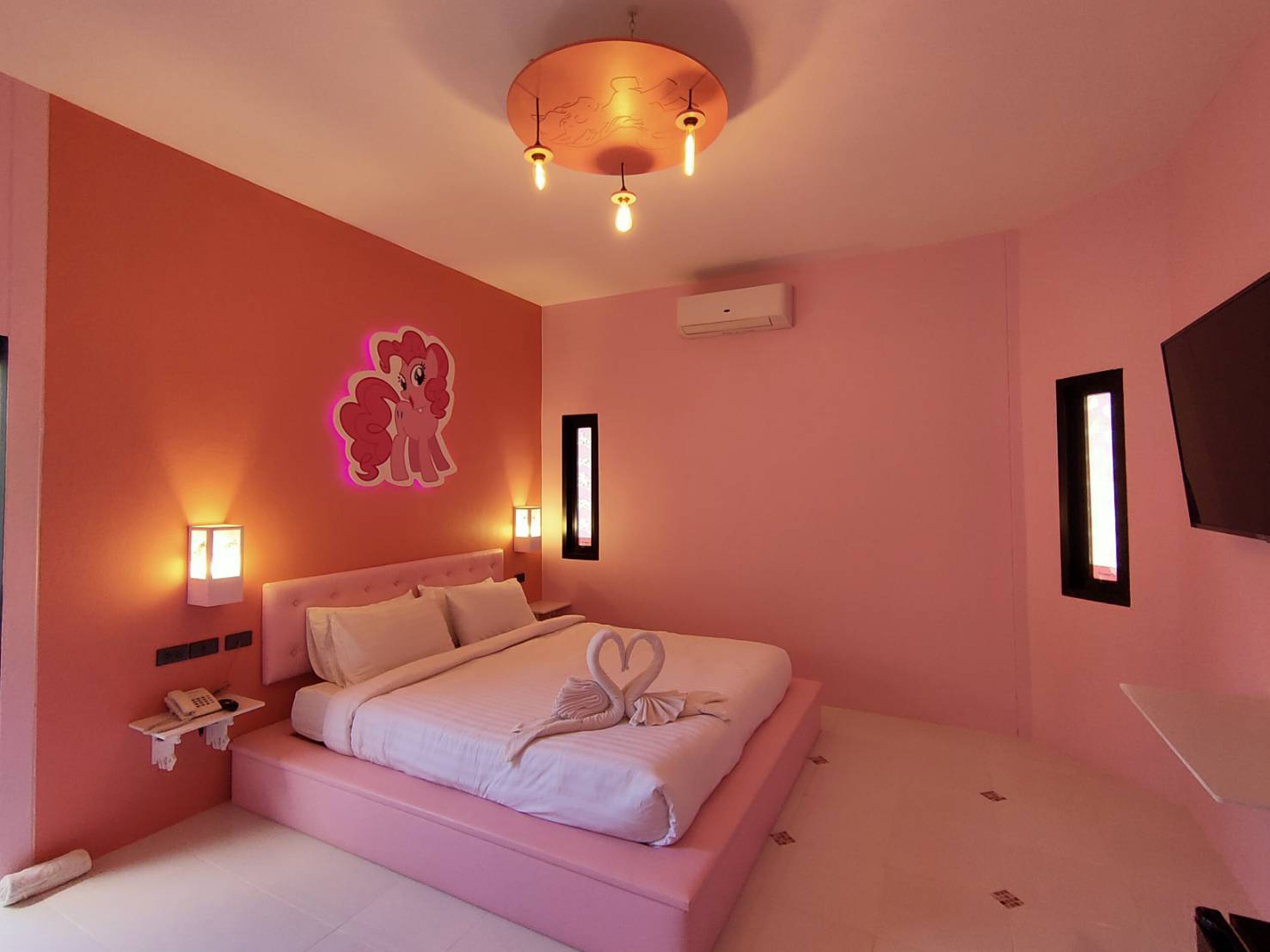 Camera d'albergo in tonalità rosa con un letto, lampade da comodino, telefono a parete e televisione.