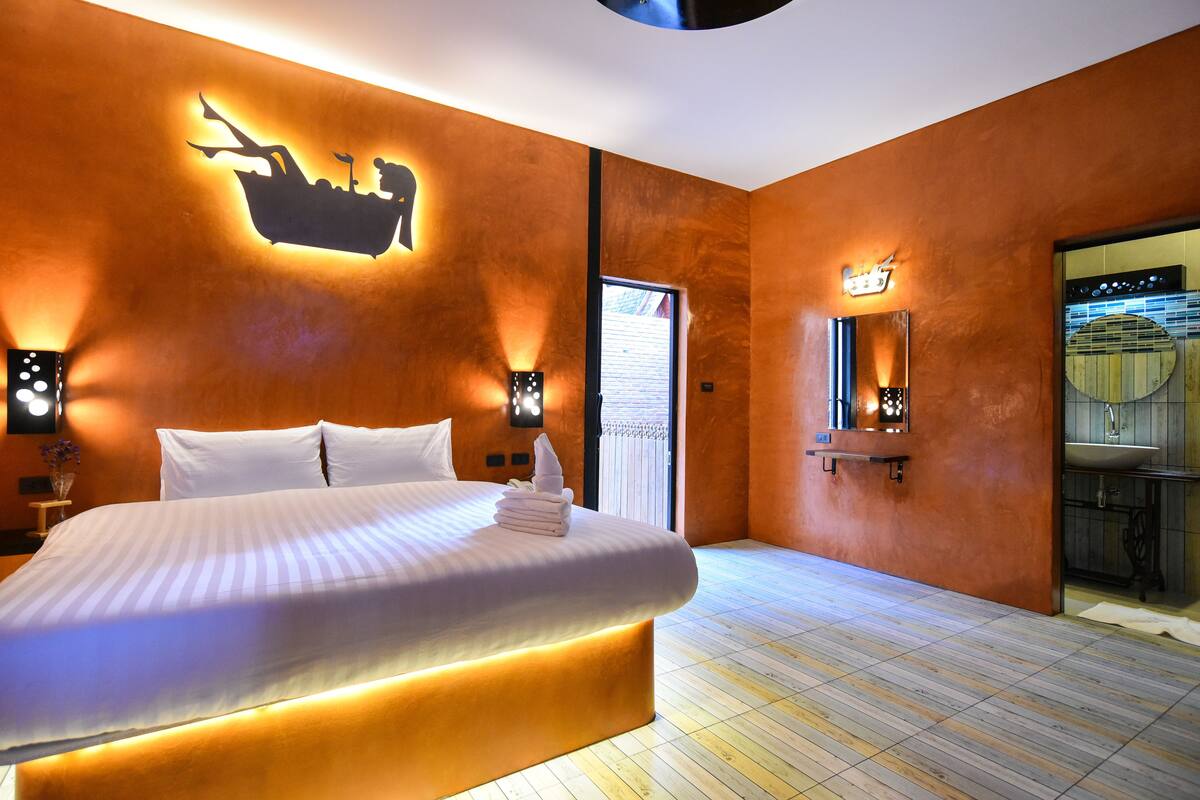 A modern hotel room with a large bed, a wall-mounted boat silhouette, and a bathroom with a large mirror.