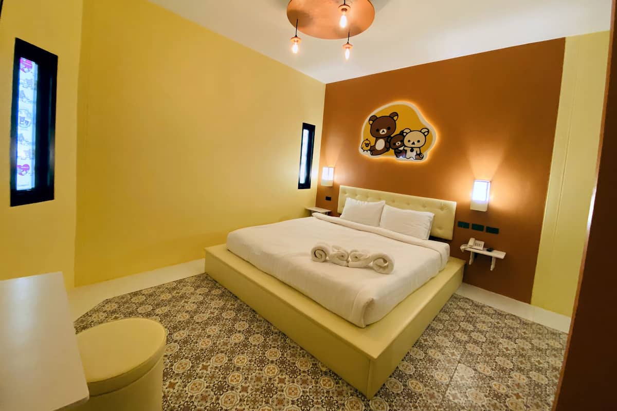 A hotel room with a bed, a bedside table, a nightstand, a wall-mounted light, a wall decoration, and a patterned floor.