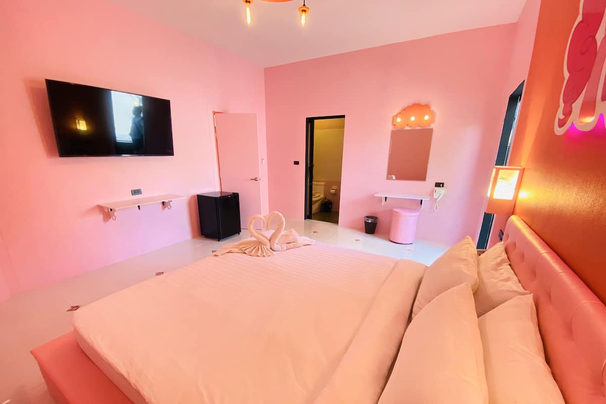 A hotel room with a large bed, a flat-screen TV mounted on the wall, a bedside table, a mirror, and a small cabinet.