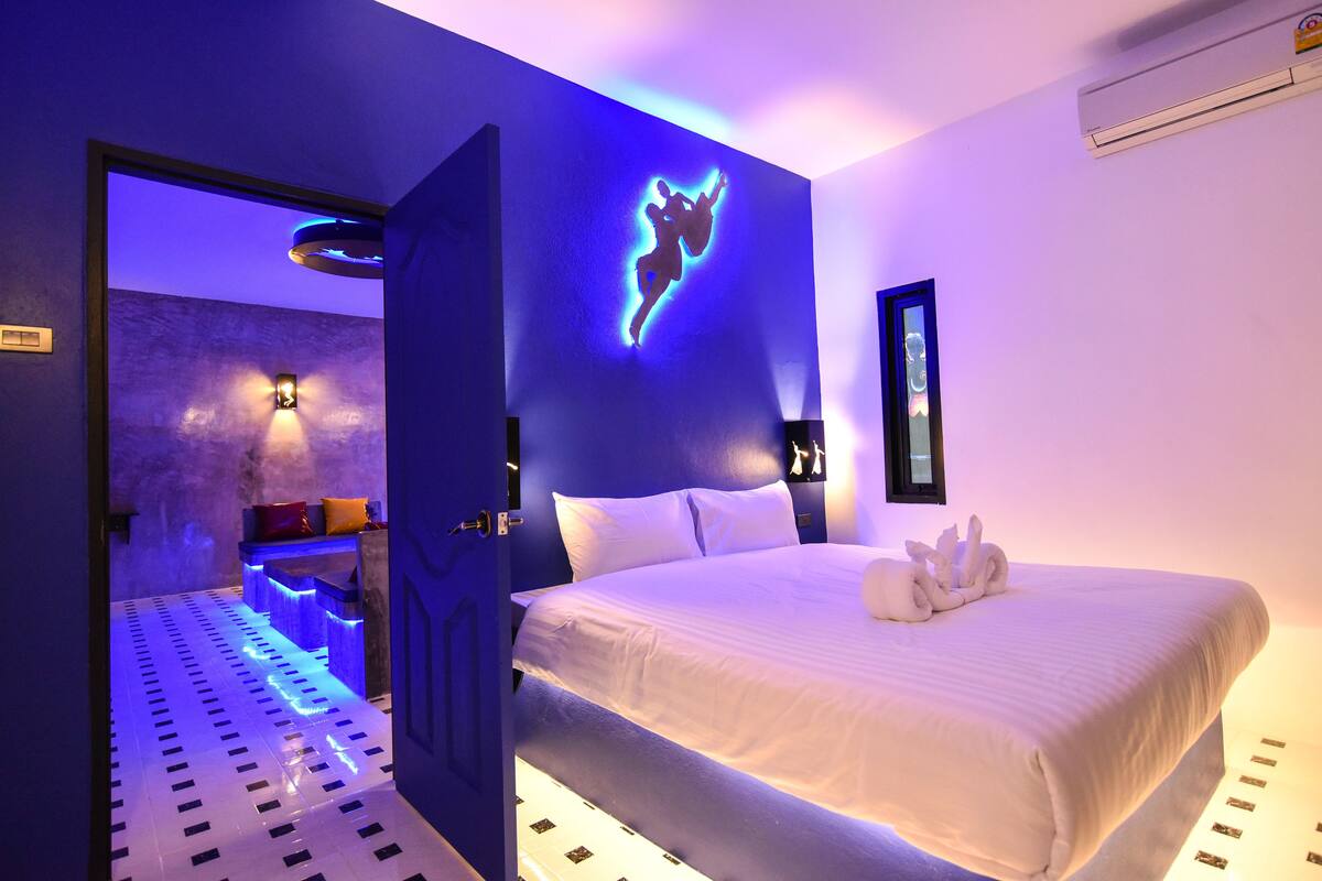 A modern hotel room with a bed, a wall-mounted light fixture, and a door leading to another room.