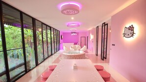 A modern interior with a long table and pink chairs, a white sofa, and a Hello Kitty wall decoration. - Bed Villa Resort Chaing Rai (Chiang Rai)
