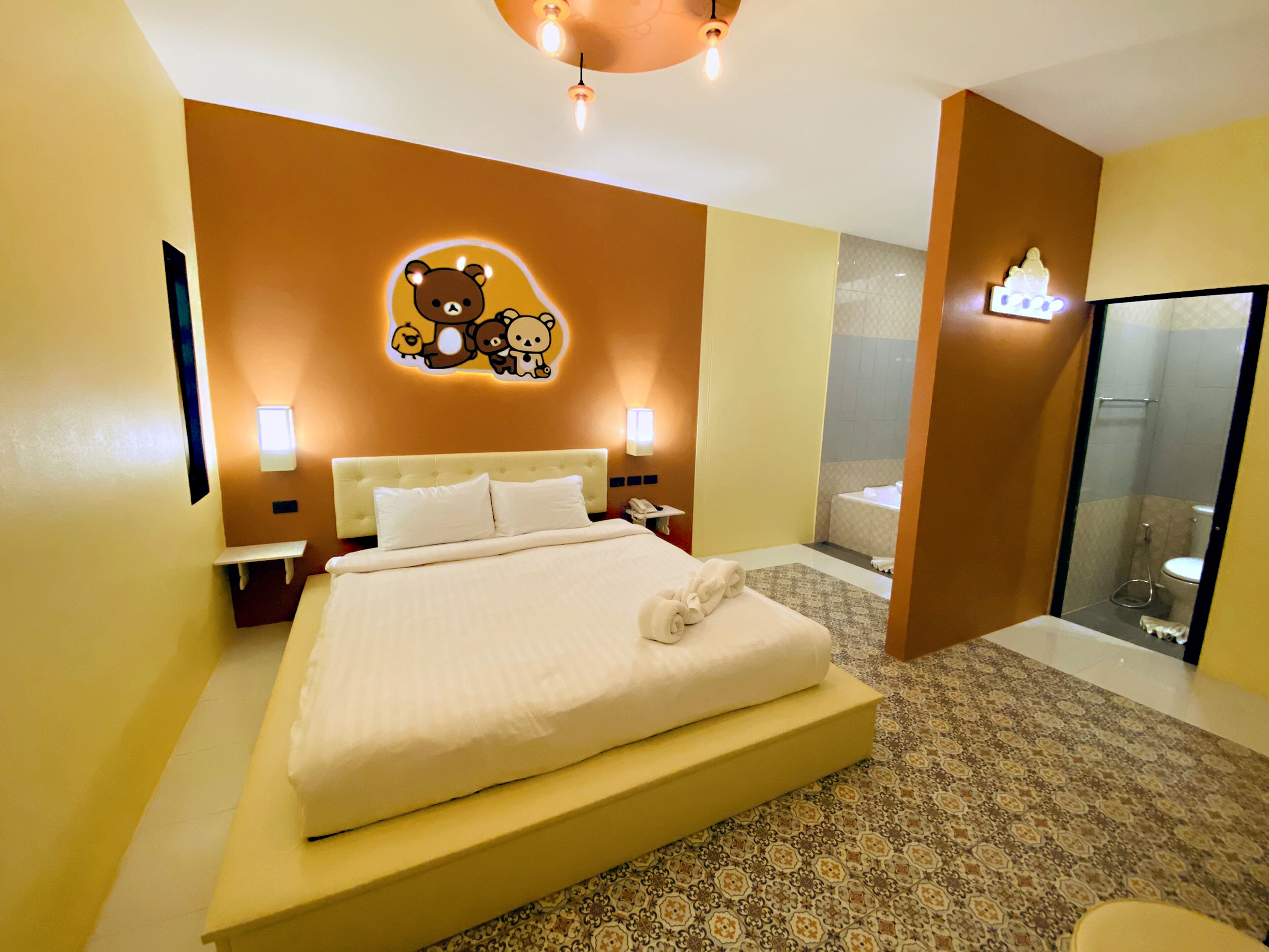 Quarto de hotel com uma cama grande, uma decoração temática de urso na parede, banheiro com banheira e box de vidro.