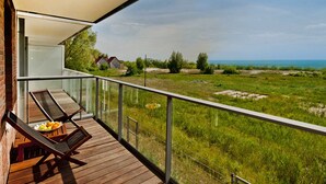 A balcony with wooden flooring and two lounge chairs, overlooking a grassy field and a body of water.