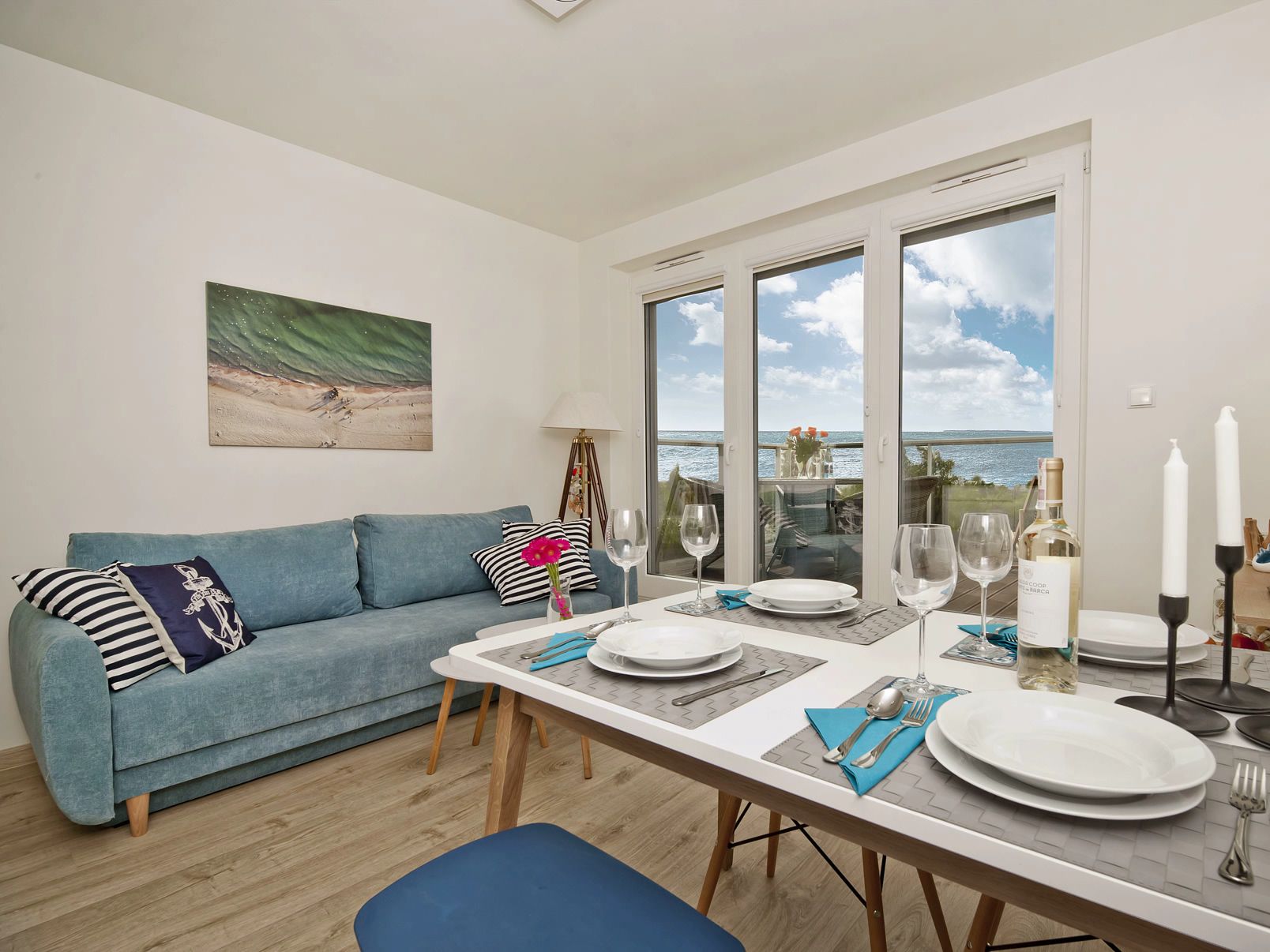 A dining area with a table set for two, a blue sofa, and a painting on the wall.