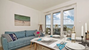 A dining area with a table set for two, a blue sofa, and a painting on the wall.