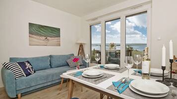 A dining area with a table set for two, a blue sofa, and a painting on the wall.