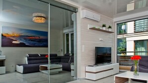 Ein modernes Wohnzimmer mit Glastrennwand, einem Flachbildfernseher und einem Gemälde vom Sonnenuntergang.