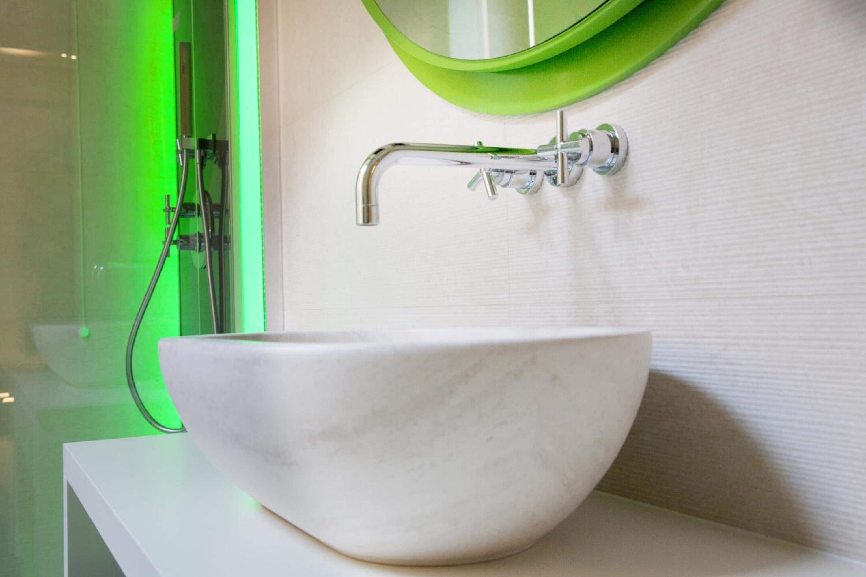 A white marble sink with a green mirror above it, mounted on a white wall.