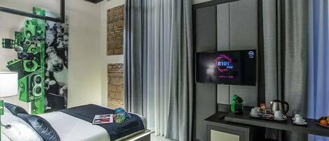 Una habitación de hotel moderna con una cama, un televisor, un escritorio con cafetera y una pared con un diseño abstracto en tonos verde y negro.