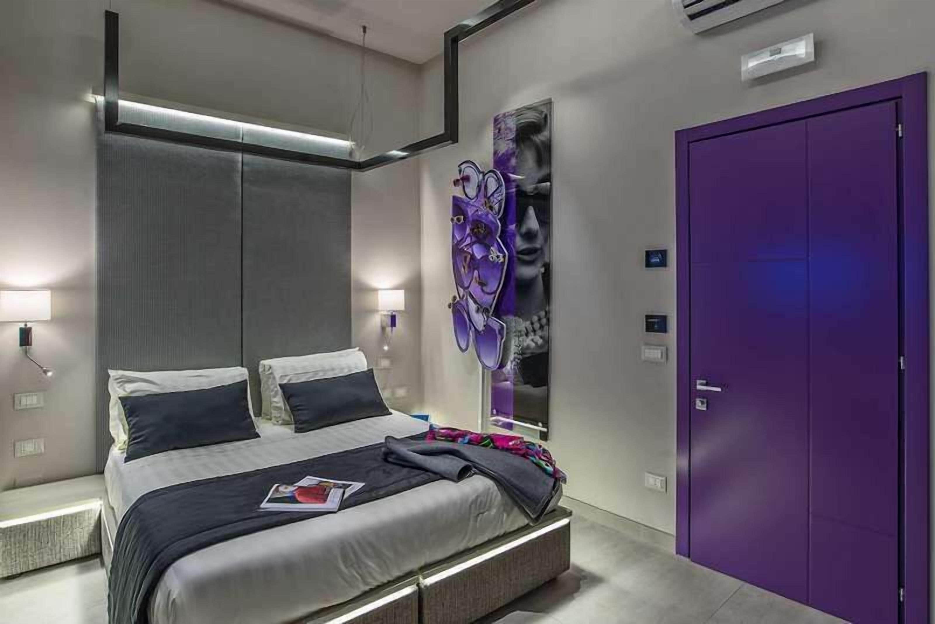 Una camera da letto moderna con un letto, lampade da comodino, un armadio viola e un'opera d'arte a parete.