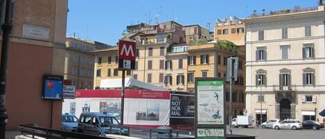 A street view with a red and white sign for a hotel, a white van, and a building with multiple windows and balconies.