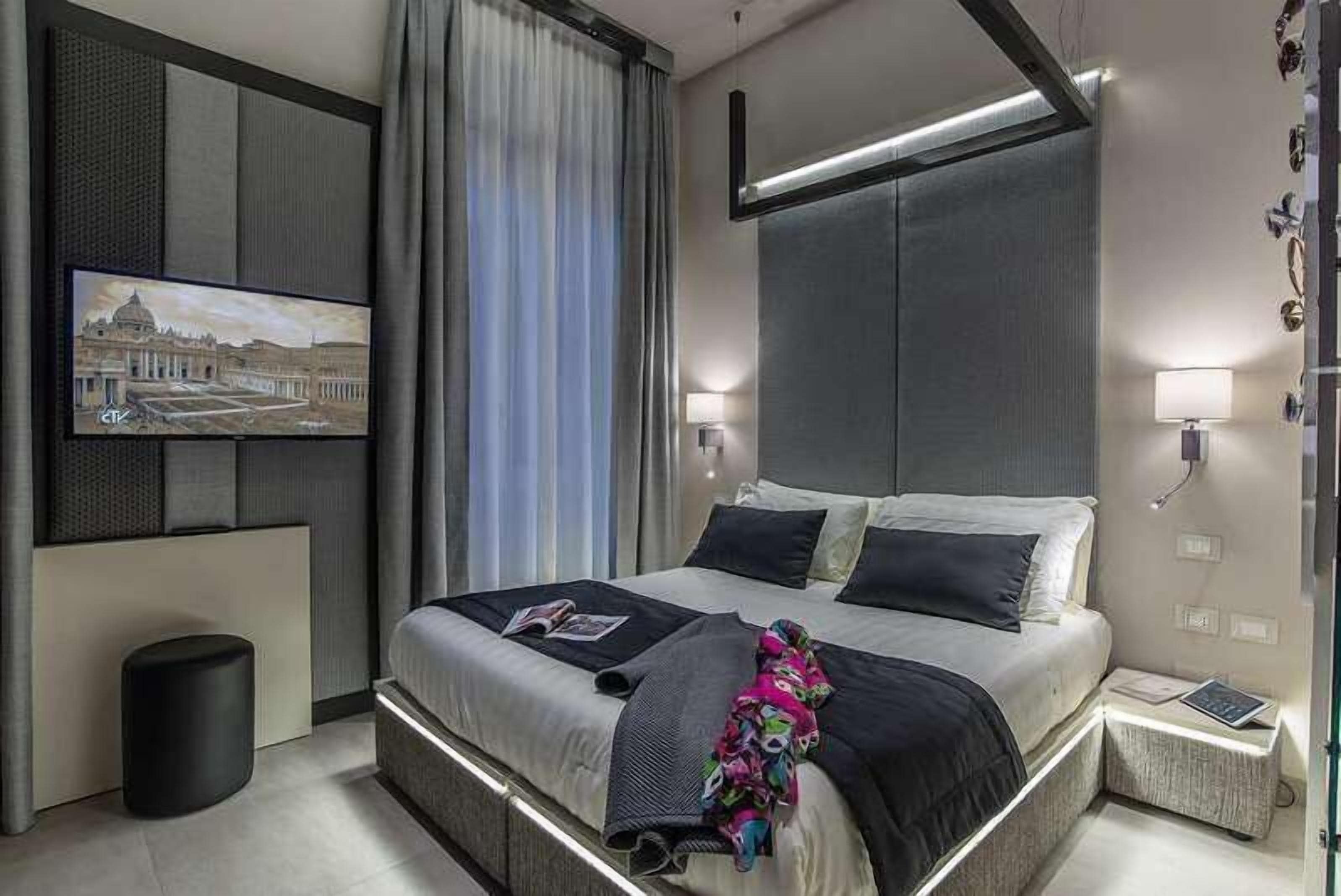 Ein modernes Hotelzimmer mit einem großen Bett, einem flachbildfernseher an der Wand und einem Nachttisch mit einer Lampe.