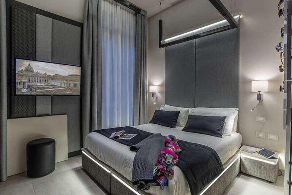 Una habitación de hotel moderna con una cama grande, un televisor de pantalla plana en la pared y una mesita de noche con lámpara.