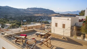 A rooftop terrace with sun loungers, a small table, and a view of a valley and mountains. - Residenza Maria Lindos Villa (Rhodes)