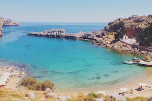 A coastal area with clear turquoise waters, rocky terrain, and a small white building near the shore.